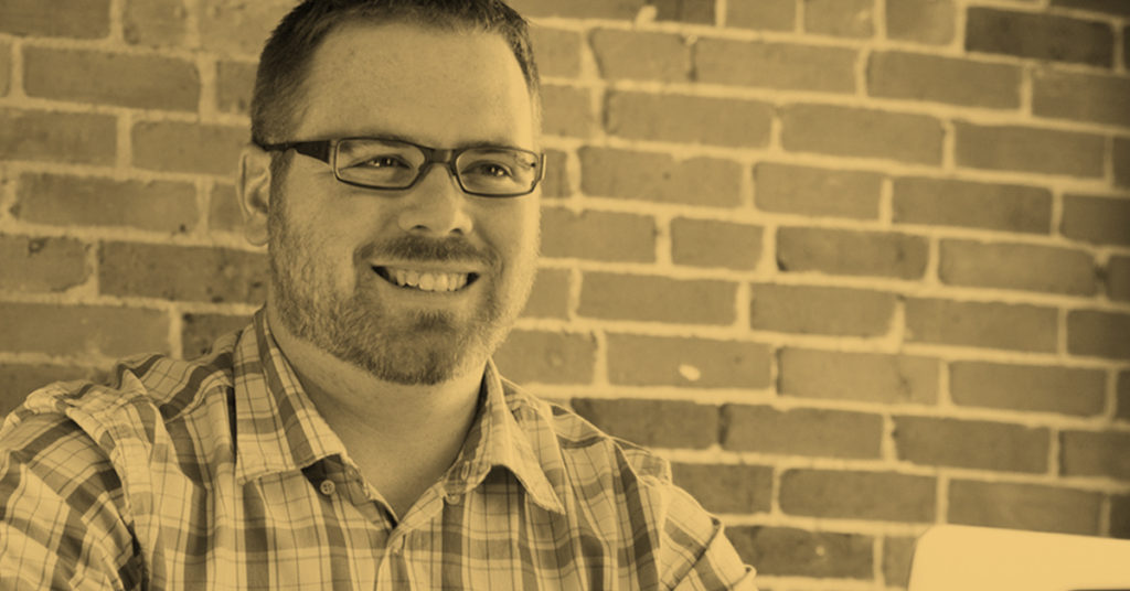 man smiling with brick wall behind him